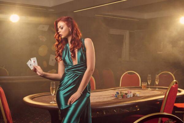 attractive-redheaded-girl-long-blue-satin-dress-is-posing-with-two-aces-her-hand-against-poker-table-luxury-casino-passion-cards-chips-alcohol-win-gambling-it-is-as-female-enterta-scaled